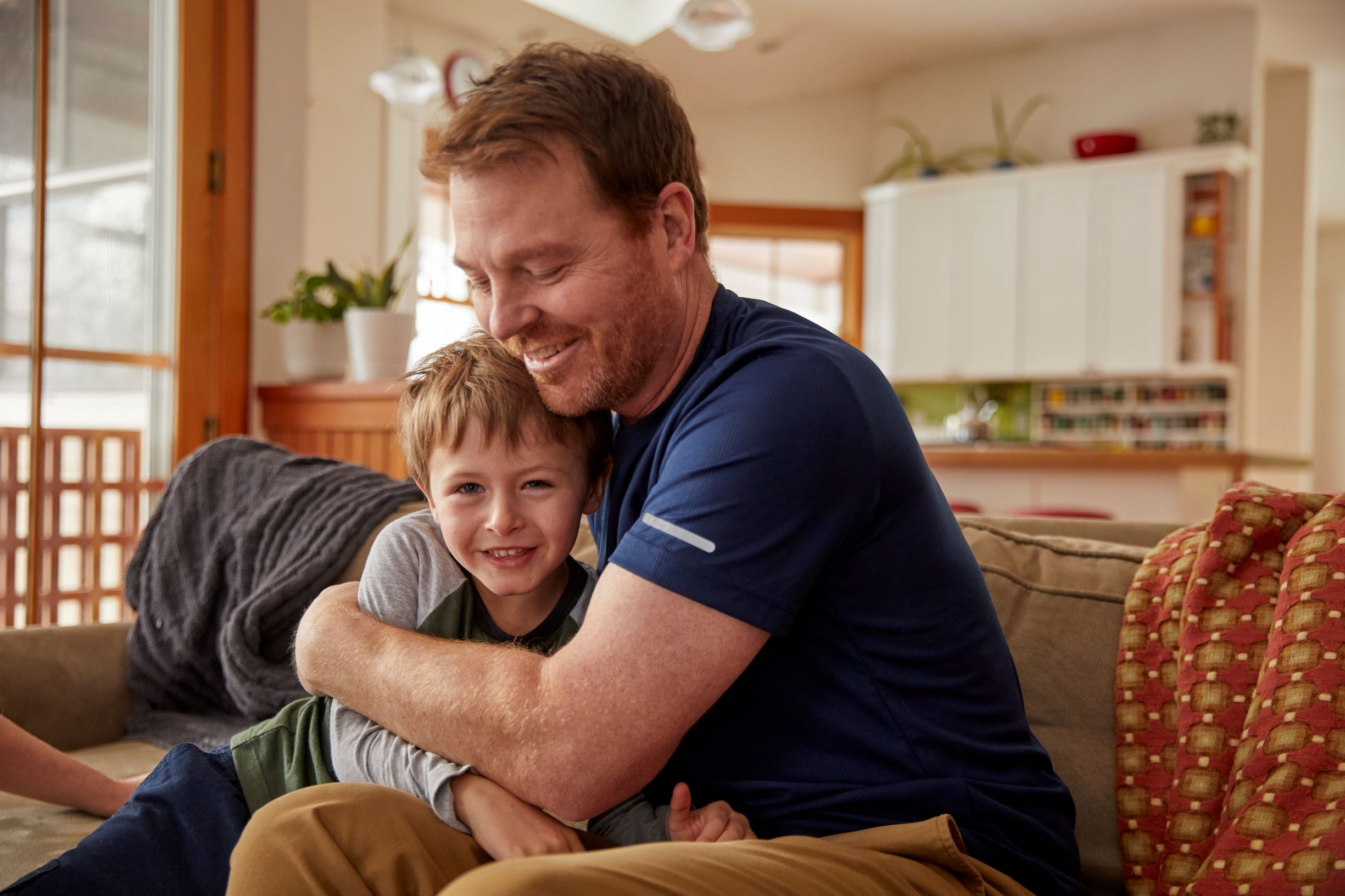 A man sitting on a couch at home hugging his son.