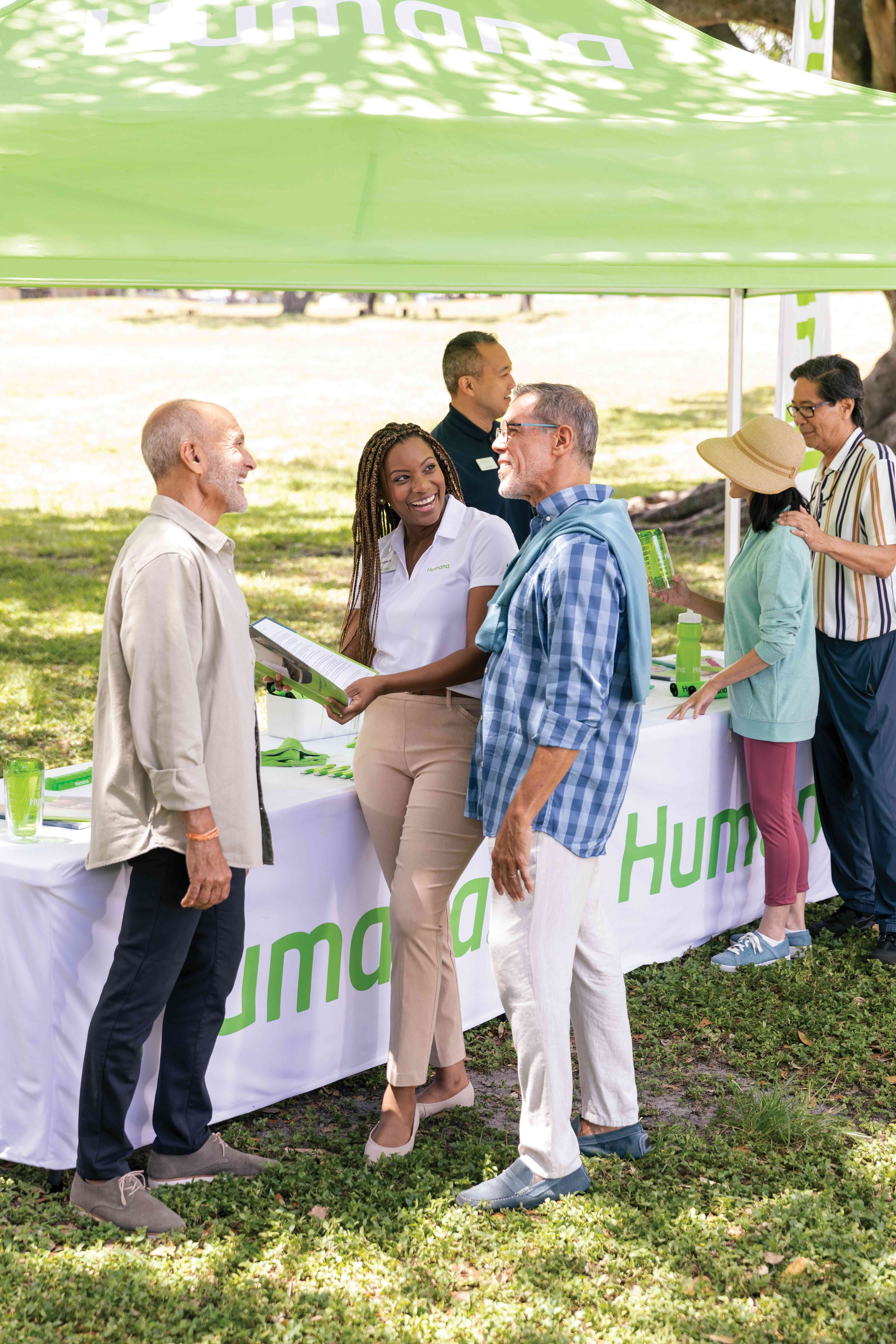 Humana associates gathered at a table outdoors with company promotional items smiling and conversing.