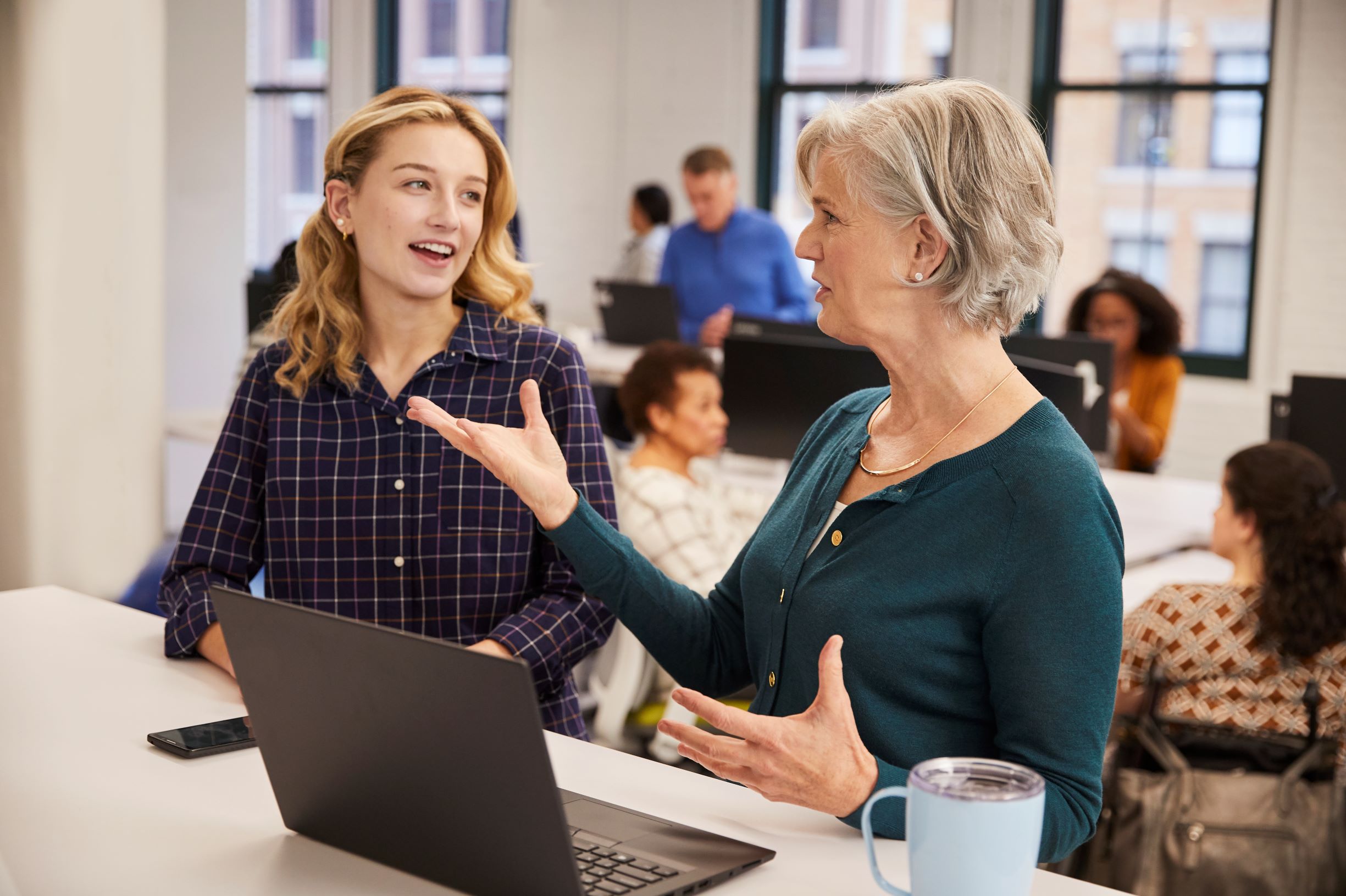 Two female Humana employees having a conversation in an office near a computer.