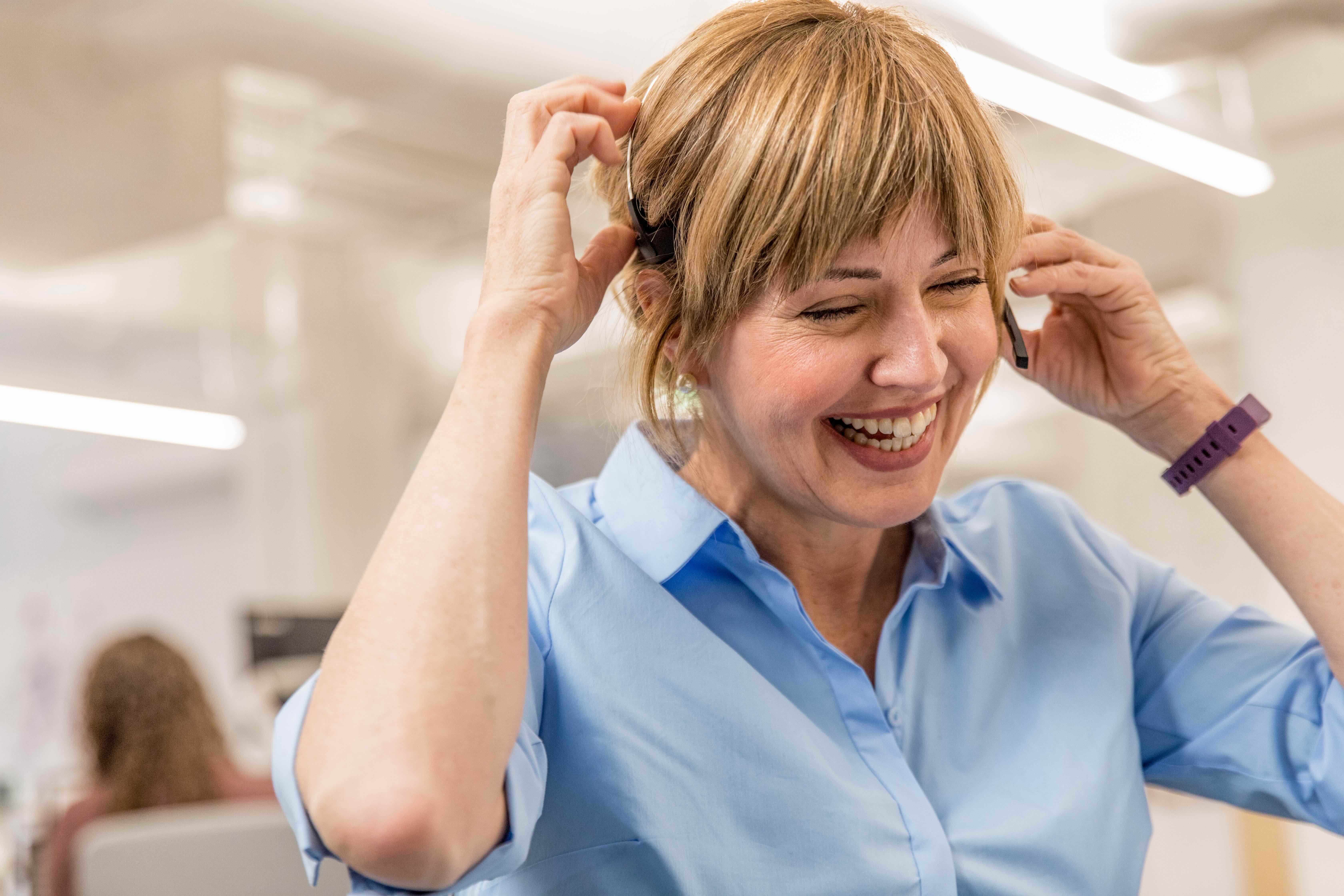 A woman smiling while adjusting her headset in an office.