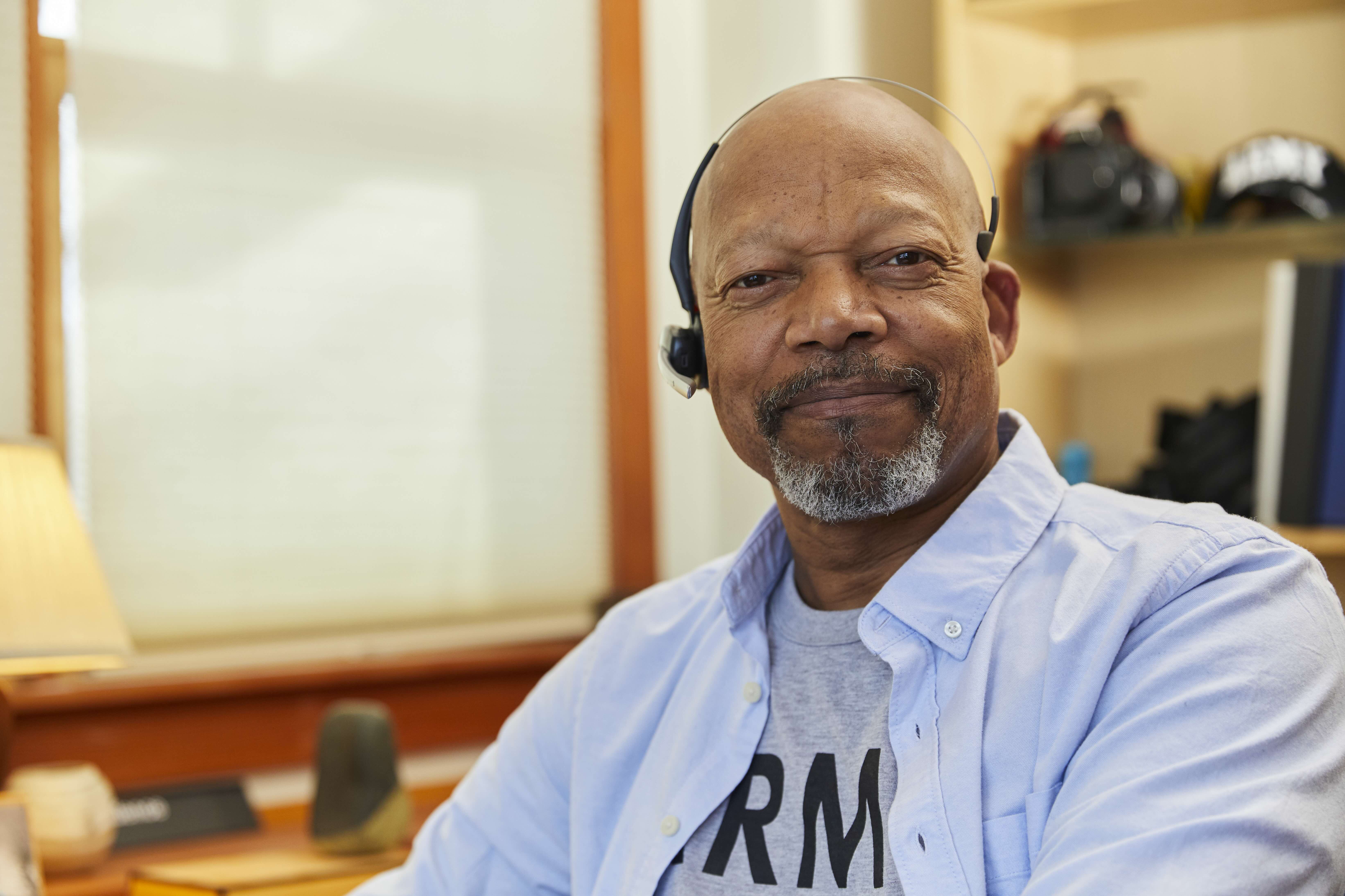 A man wearing a headset smiling while sitting in home office.