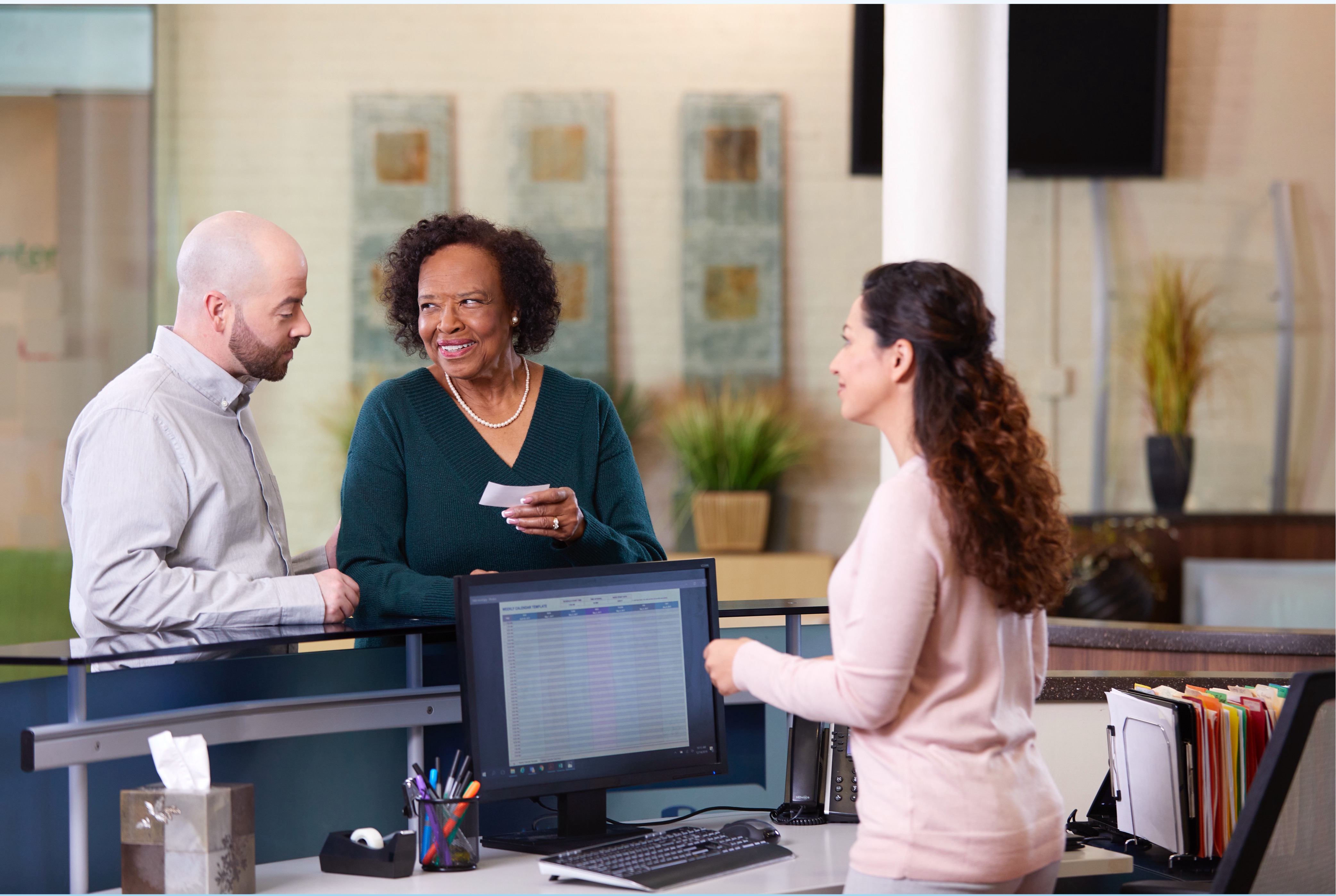 Female clinical support professional assisting an elderly couple with check-in at a clinic.