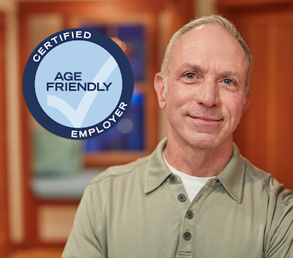 A senior male Humana employee smiling with Certified Age Friendly Employer awards badge.