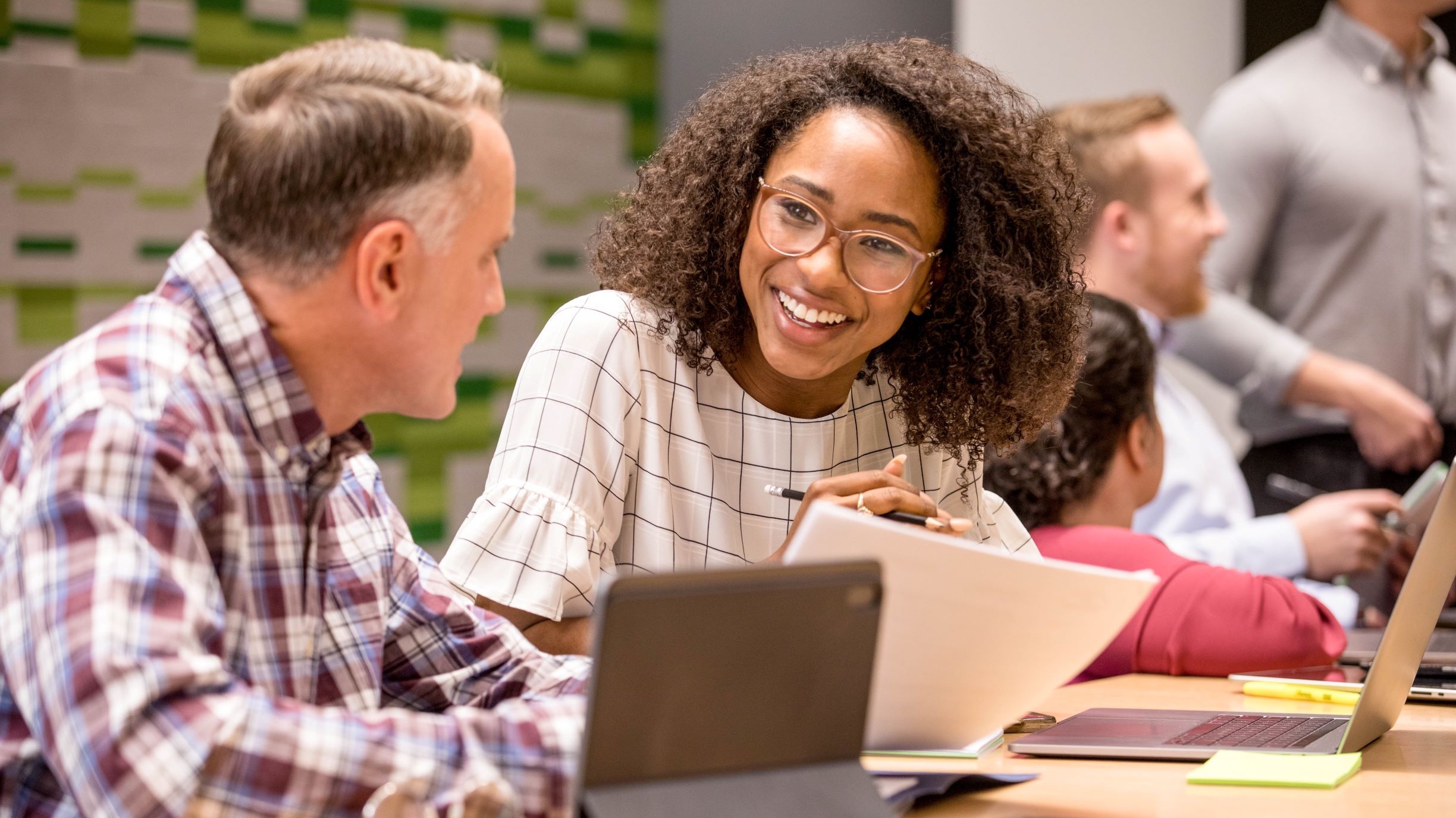 A young woman in a conference room leaning over a table smiling at other professionals.