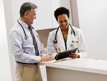 Two physicians reviewing notes and conversing in a clinic setting.