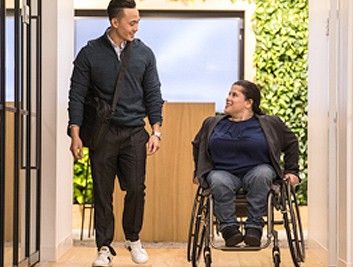 A man walking down an office hallway engaging in conversation with a woman in a wheelchair.