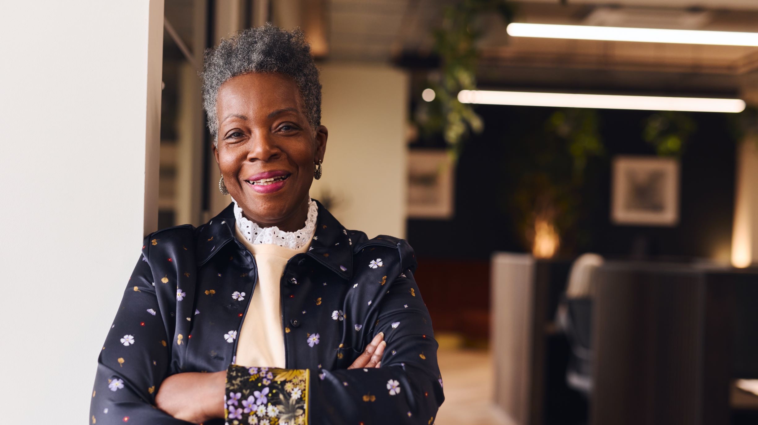 An older women stands smiling with arms crossed in an office setting.