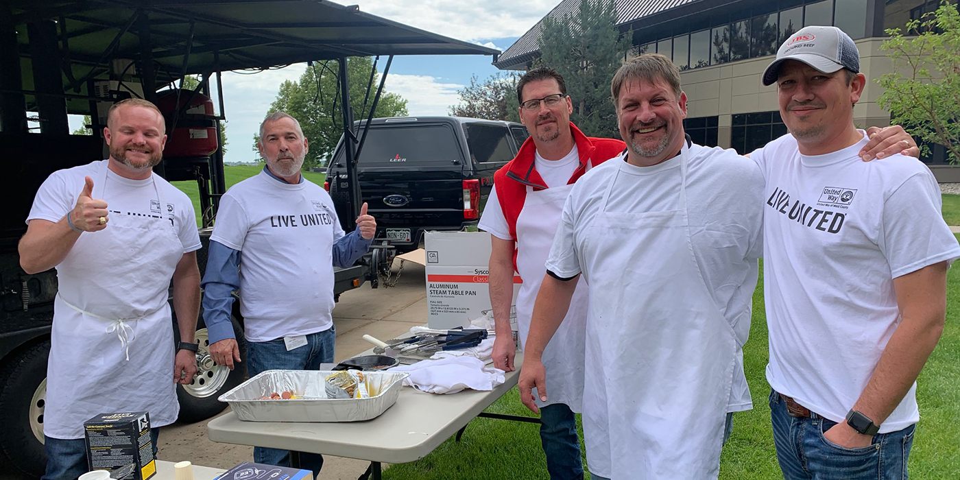 Male JBS USA team members grilling meat outside for the United Way