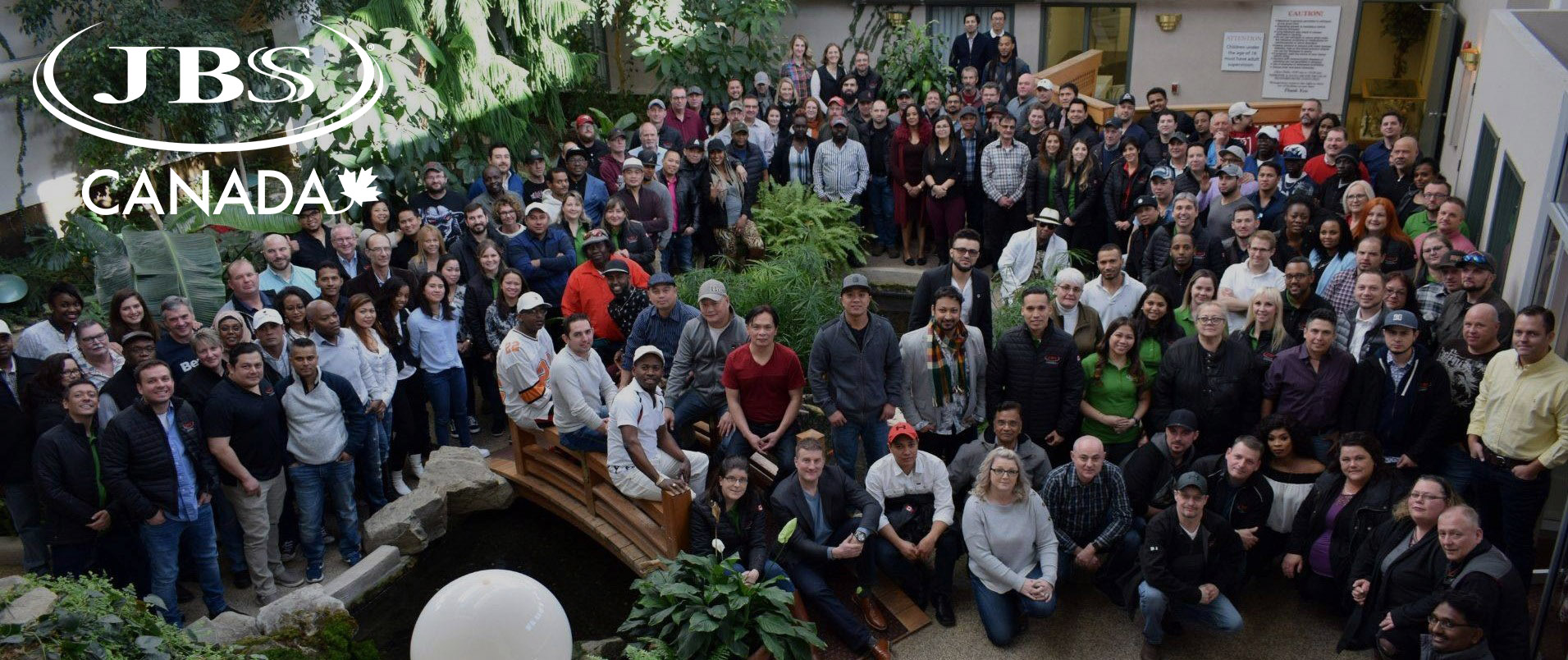 Large group of JBS Canada team members indoors with foliage