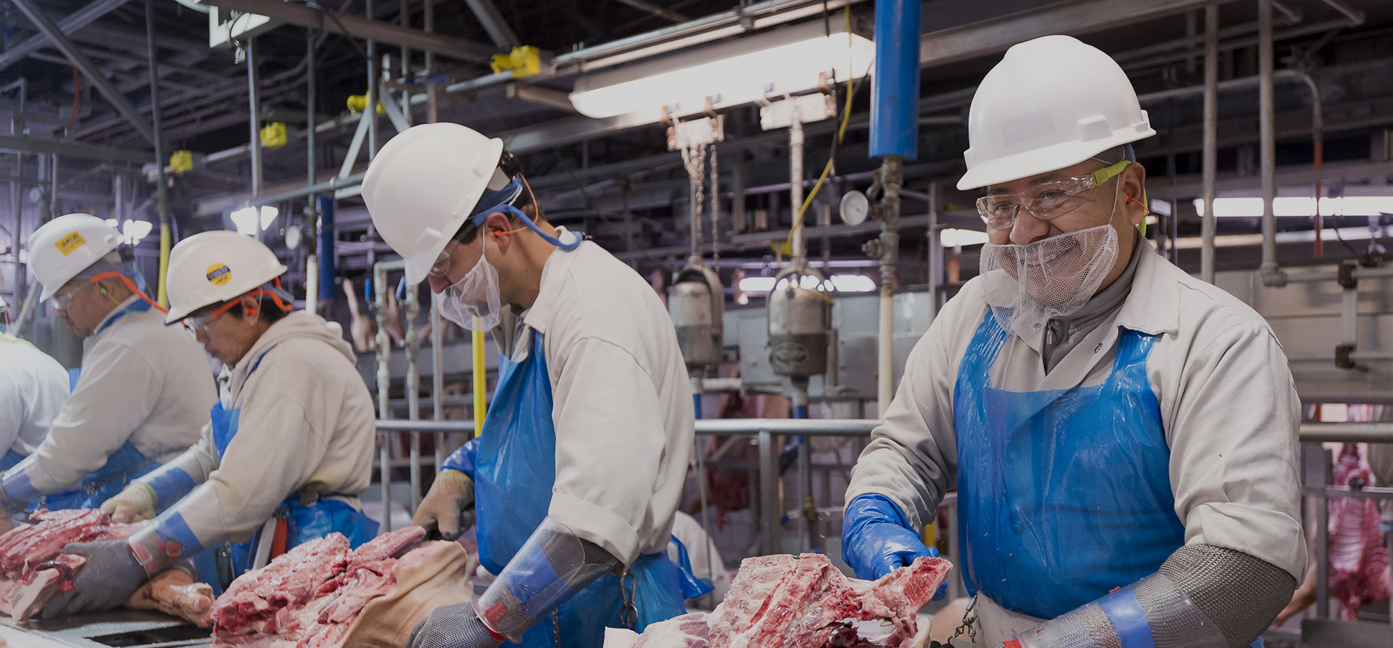 JBS USA team members in white frocks and hard hats cutting meat in a plant