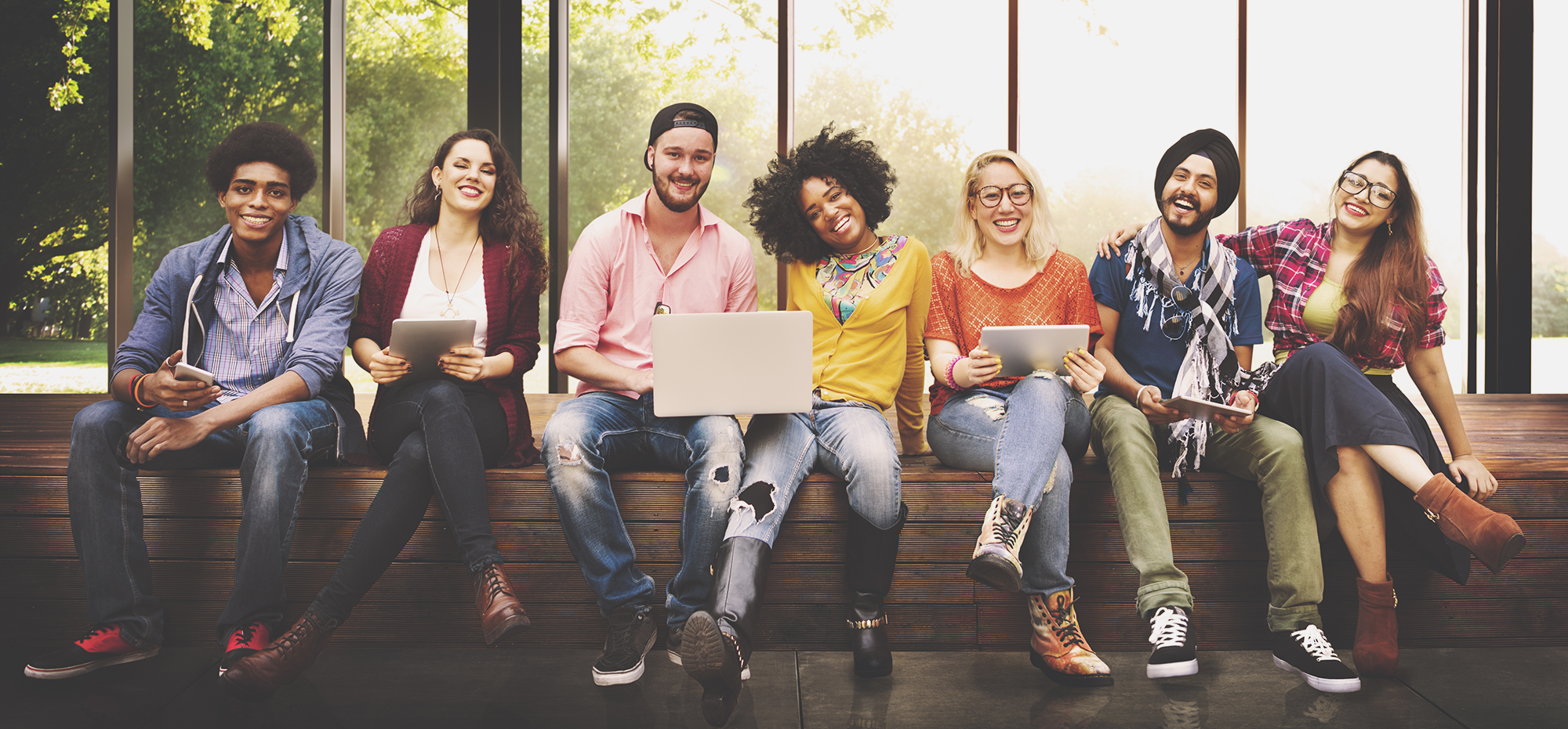 College students sitting in a row in front of green trees