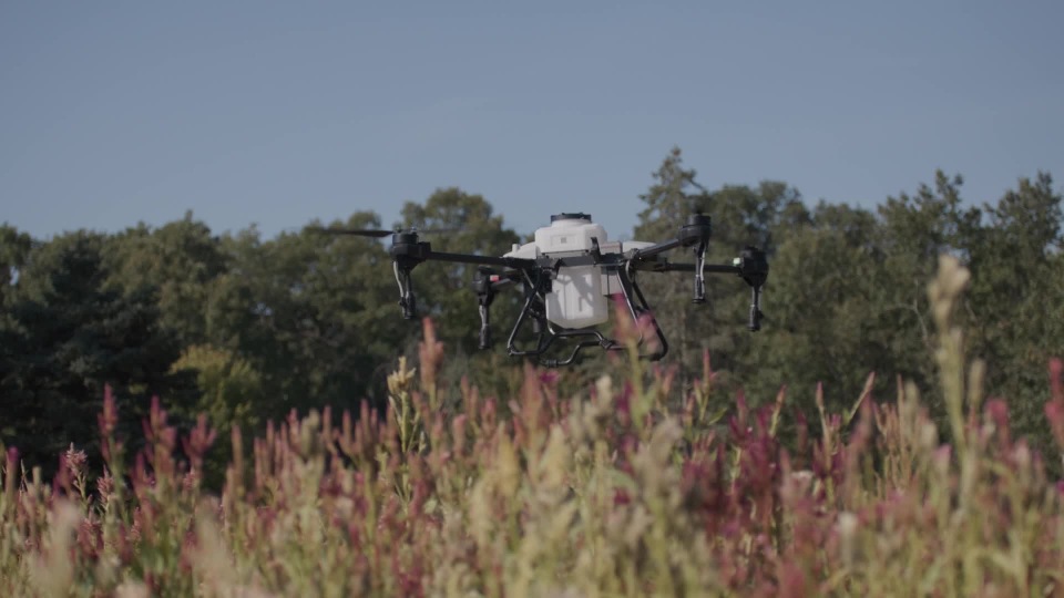 Industrial drone hovering above tall grass in an outdoor field, used for aerial data collection and monitoring.