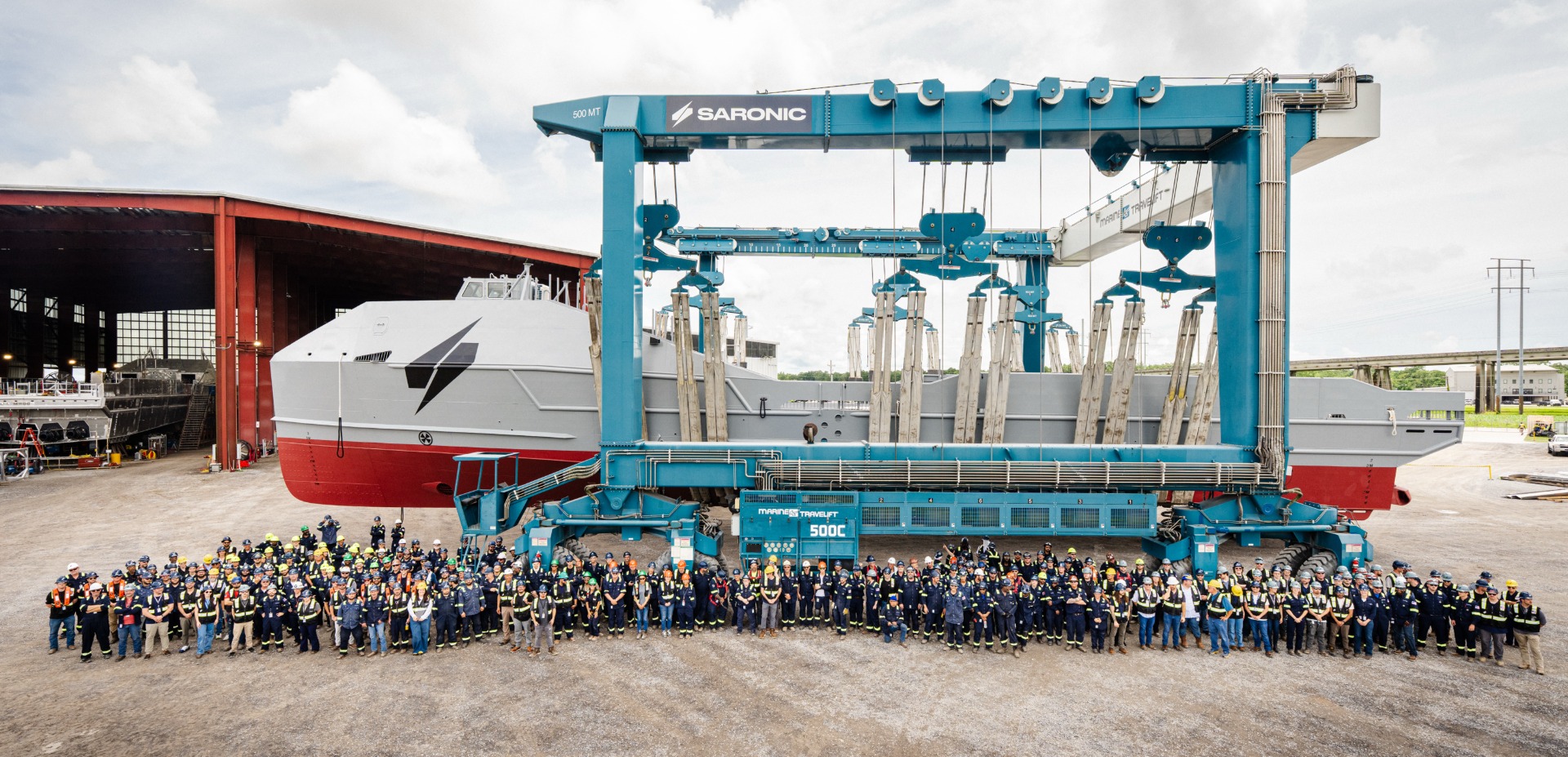 Large group of shipyard employees standing in front of a marine vessel and heavy-duty lifting gantry at a Saronic shipbuilding facility.