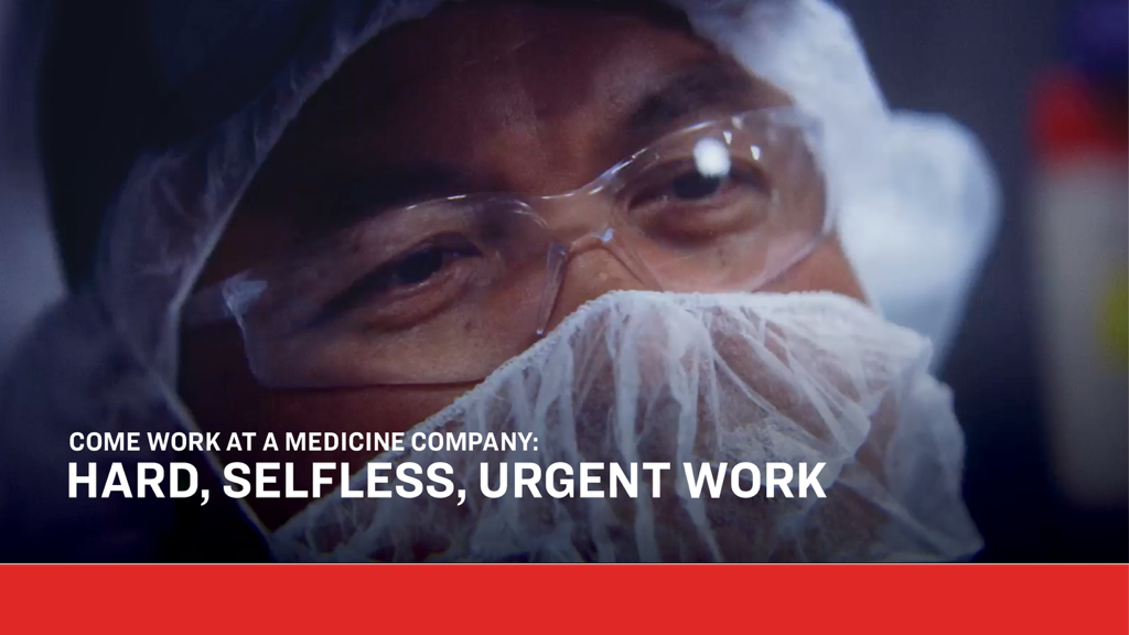 Close-up of a lab professional in full protective equipment—goggles, mask, and hair covering—working in a pharmaceutical environment. Text overlay reads: “Come work at a medicine company: Hard, selfless, urgent work,” emphasizing the critical nature of developing medicines for patients.