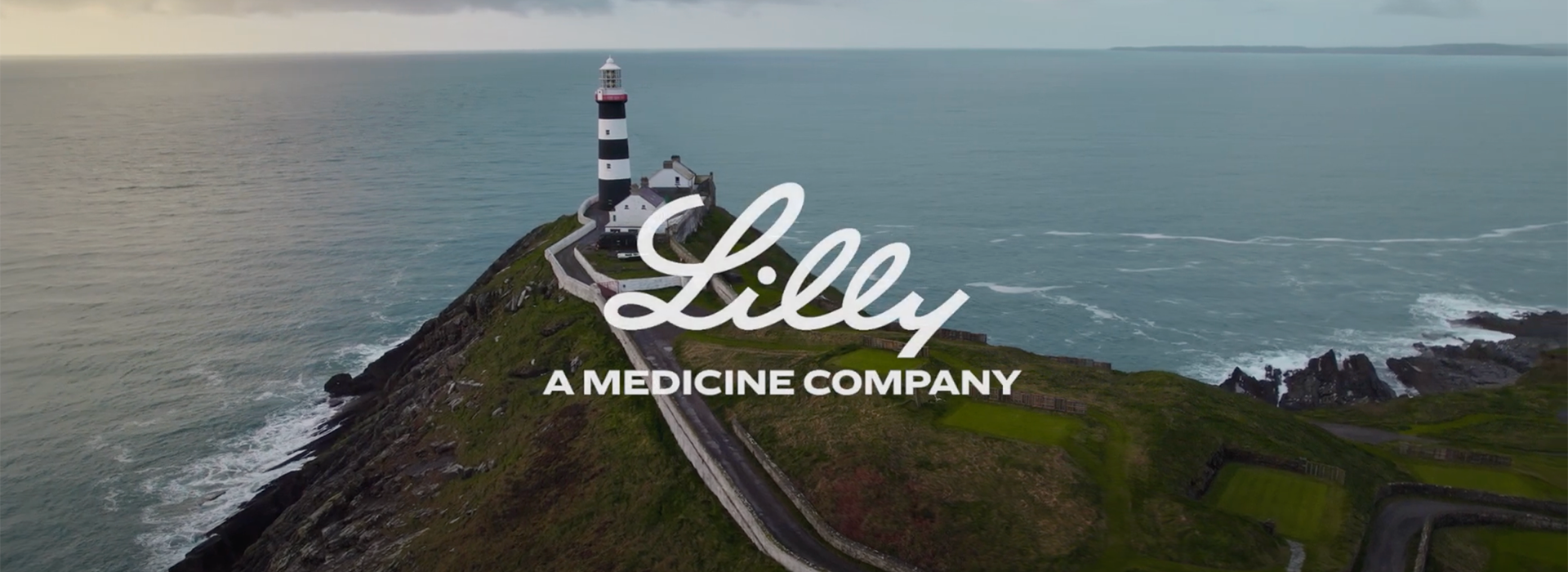 View of the coast of County Cork with a Lighthouse at the top of a cliff and the words, Lilly, A Medicine Company overlaying the image.