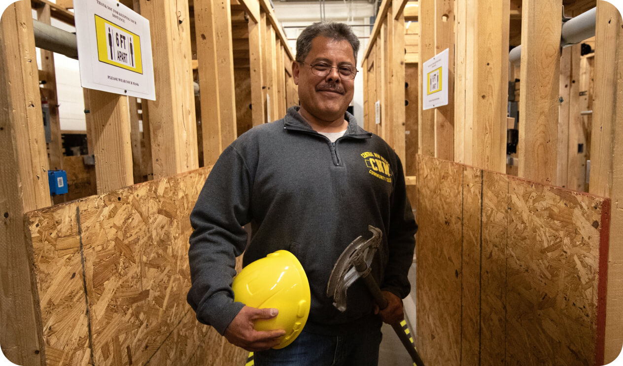Instructor standing by framed walls holding electrical equipment