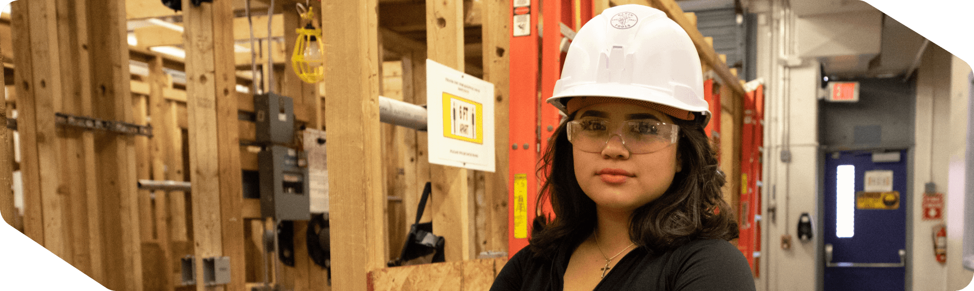 Female skilled trades student wearing protective gear standing next to a framed wall