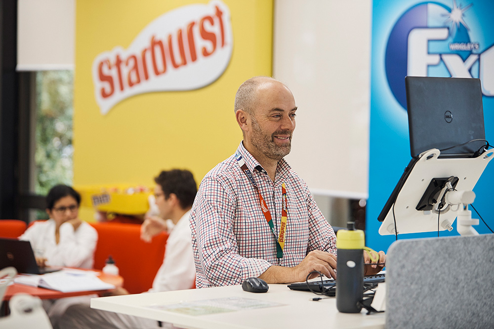 An image of a Mars Associate on their laptop in an office setting, with a bright yellow starburst background