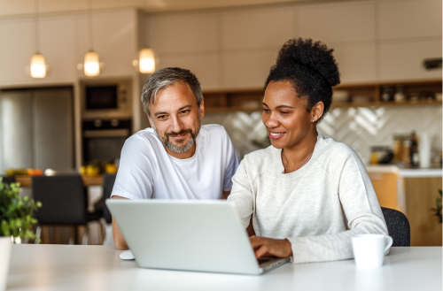 man and woman sitting by a table and sharing a laptop