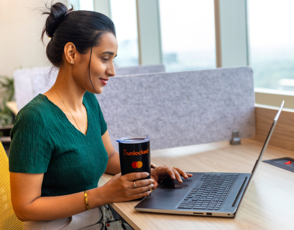 A woman sitting at a desk with a laptop and a coffee cup, engaged in remote work in a bright and open workspace. 