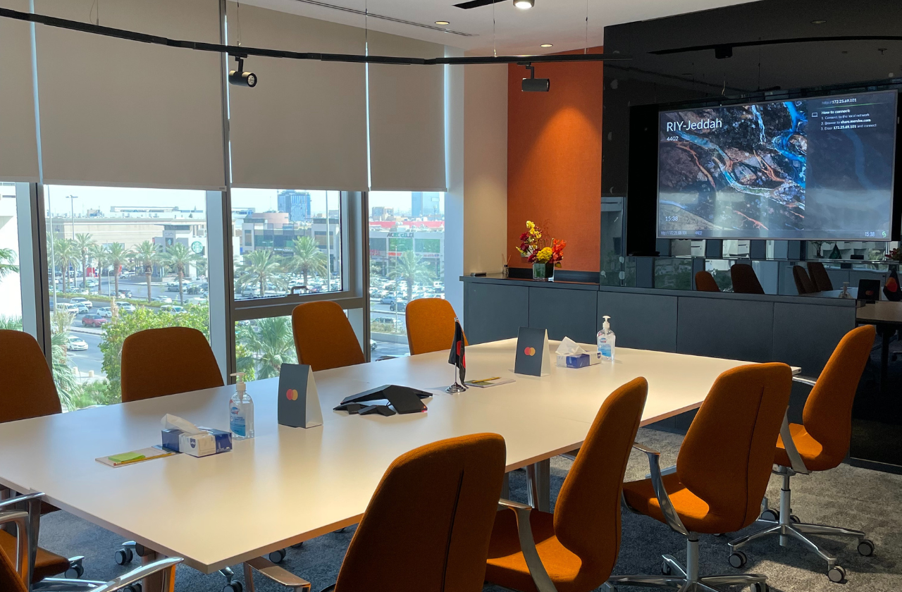 Meeting room with large screen, large white table and orange chairs