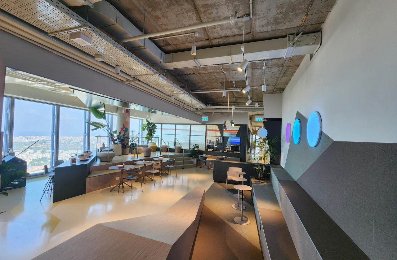 An open space area in Mastercard's Tel Aviv office, featuring various seating options, with meeting rooms visible in the background.