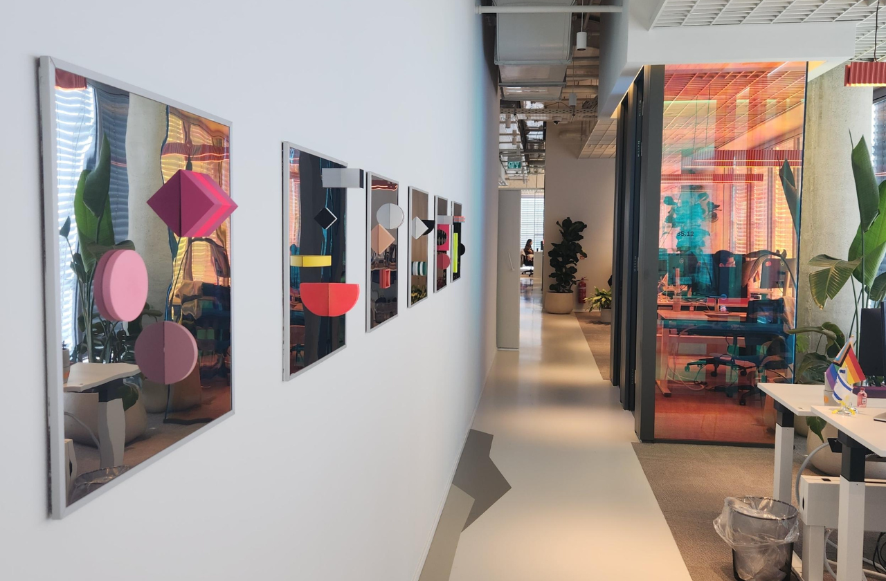 A walkway in Mastercard's Tel Aviv office, adorned with 3D wall art along the wall, with a meeting room visible in the background.