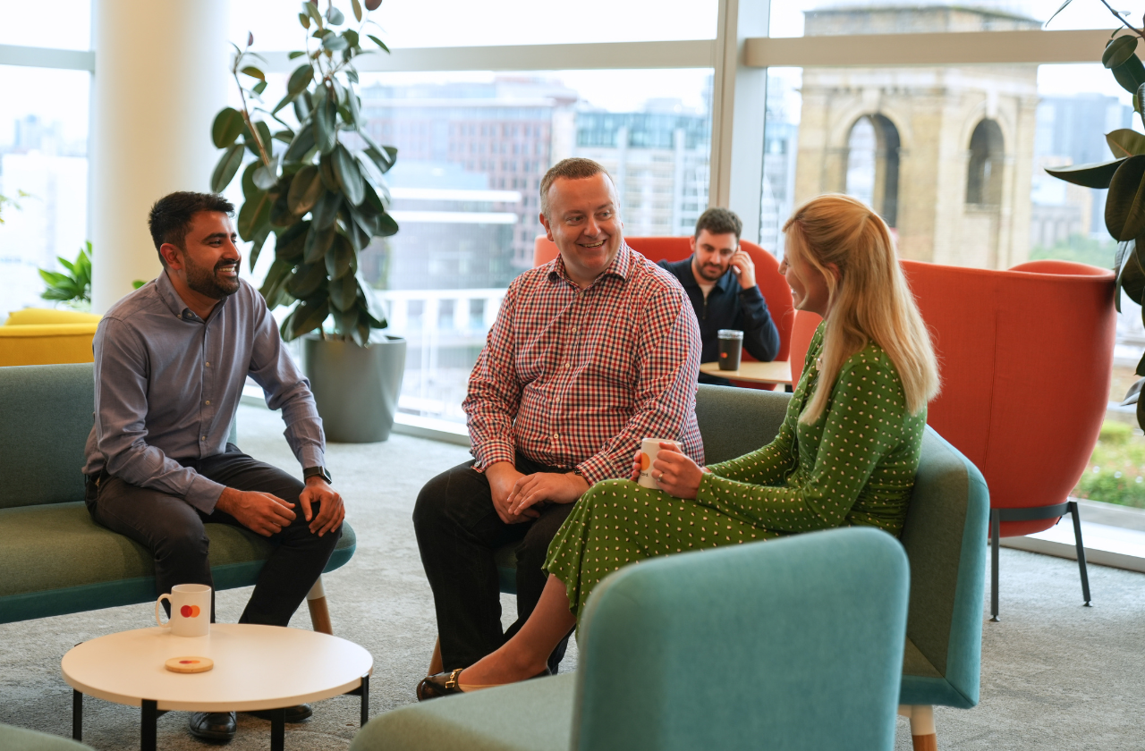 Three colleagues sitting together on blue chairs having a coffee