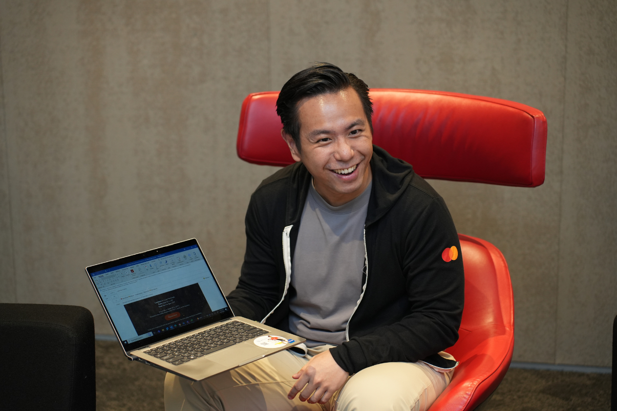 a man wearing a mastercard logo black sweater holding a computer