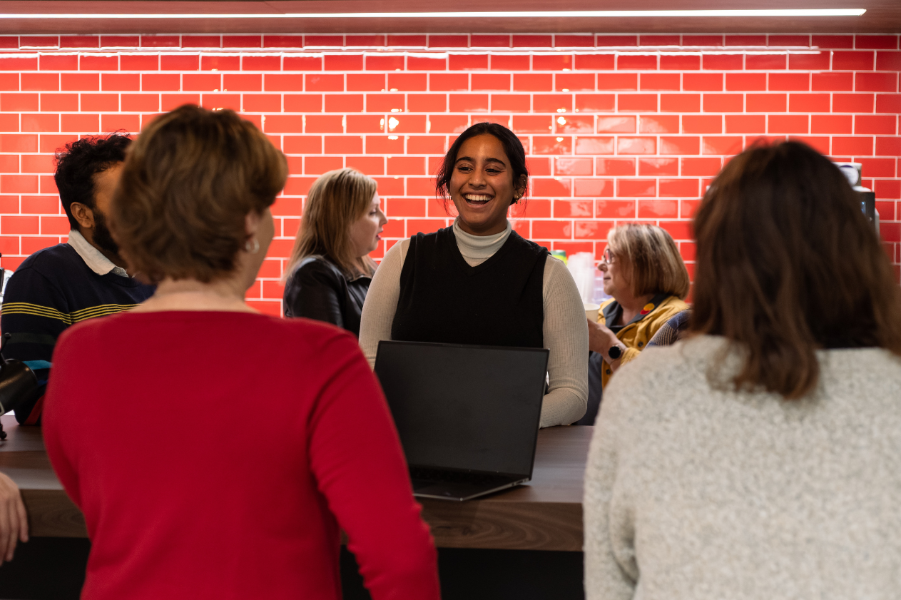 a woman smiling and laughing with her colleagues by a red wall