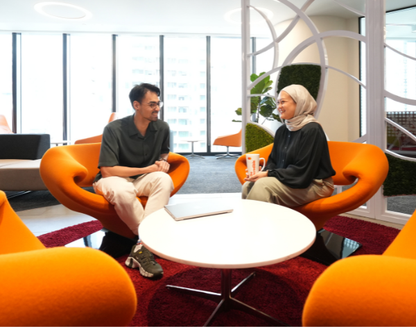 Two people having a conversation in a collaborative workspace with bright orange chairs.