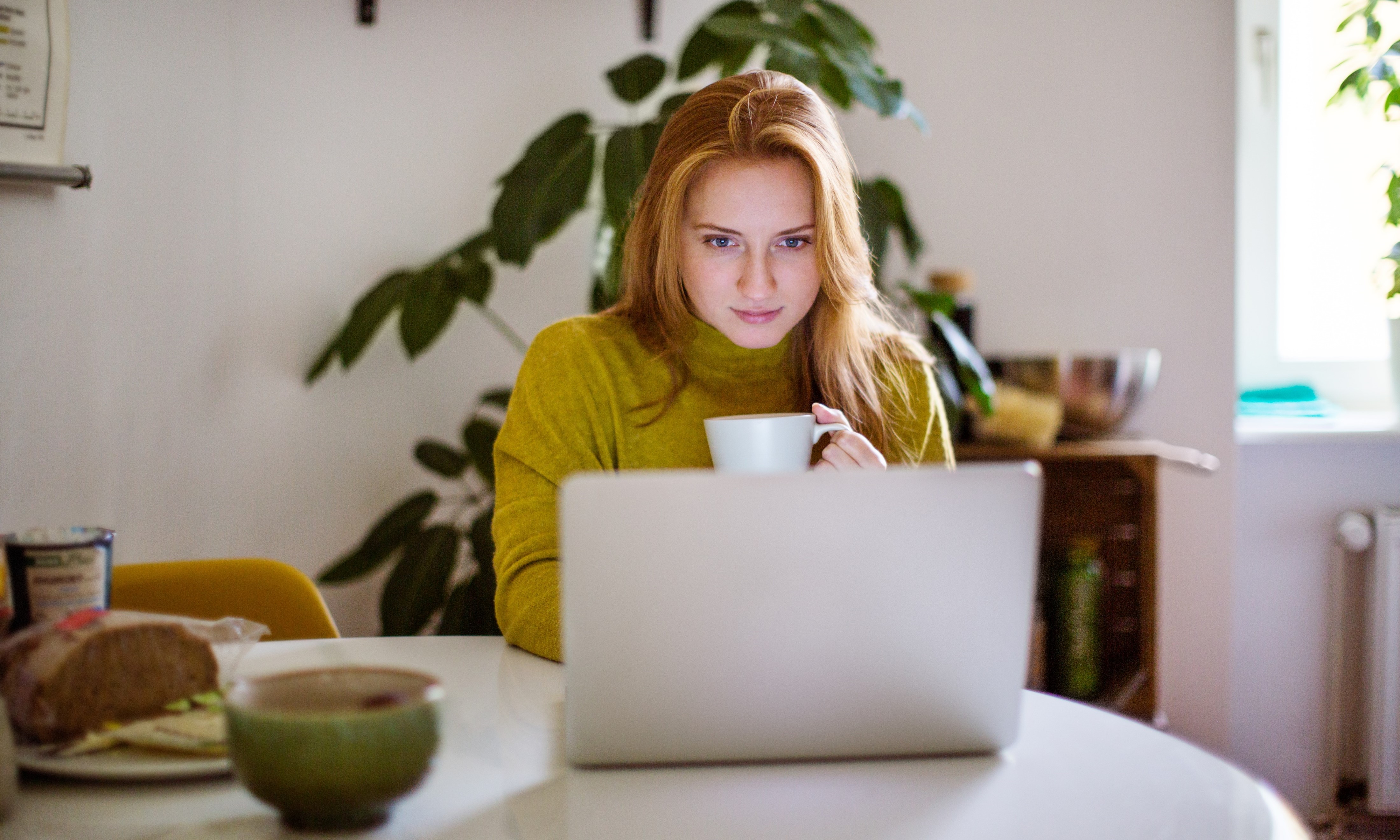 A women holding a mug while looking at laptop