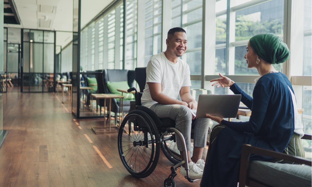 Man in wheelchair talking to women in a seat with book in hand