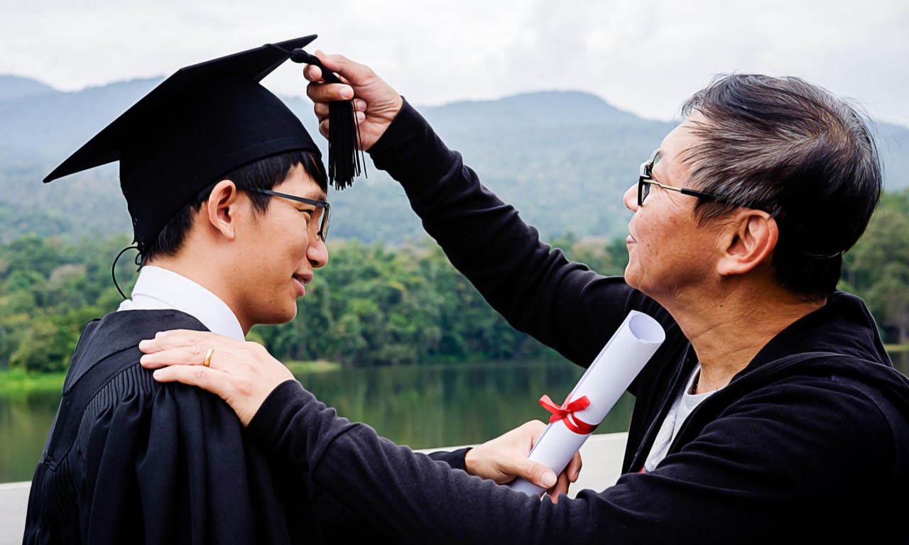 Une personne habillée d’une toge et d’un mortier tient un diplôme 