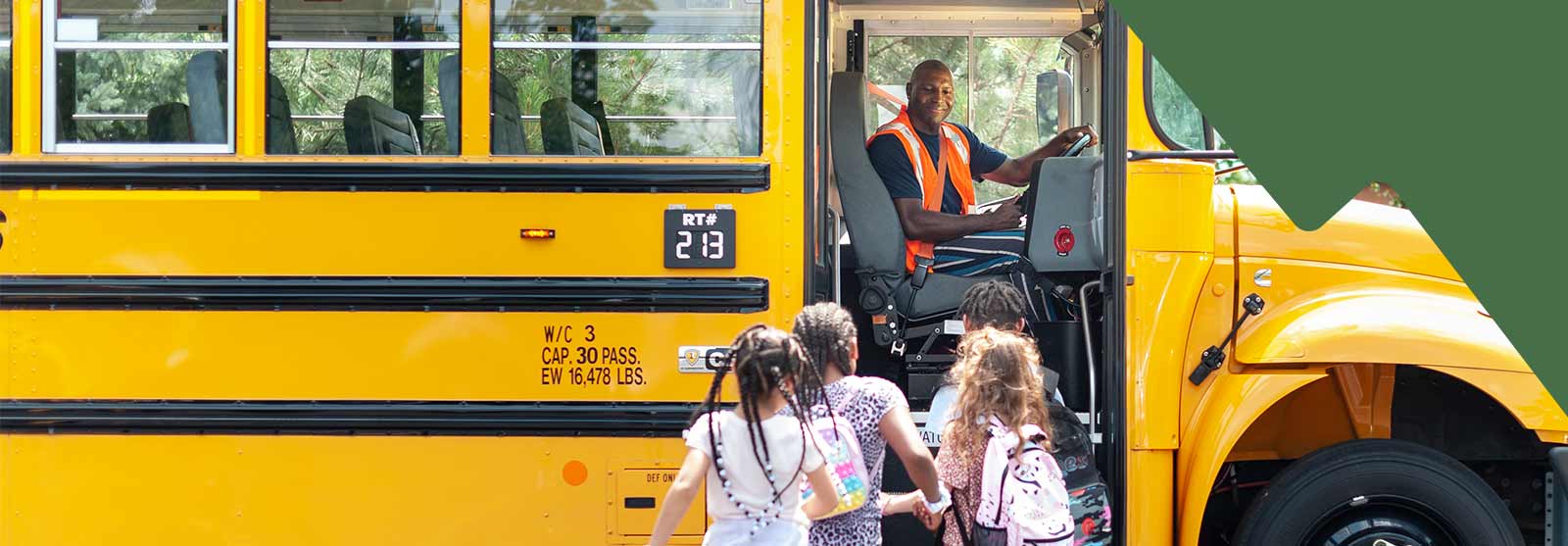 A female school bus driver smiling and standing confidently in front of a row of parked school buses, showcasing pride in her work.