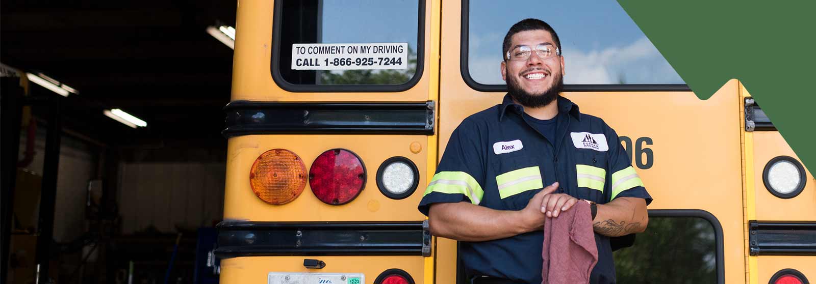 A female school bus driver smiling and standing confidently in front of a row of parked school buses, showcasing pride in her work.