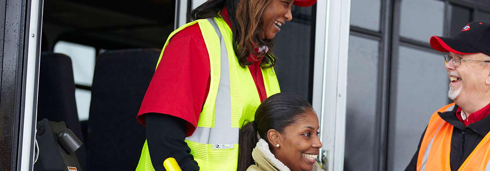 A female school bus driver smiling and standing confidently in front of a row of parked school buses, showcasing pride in her work.