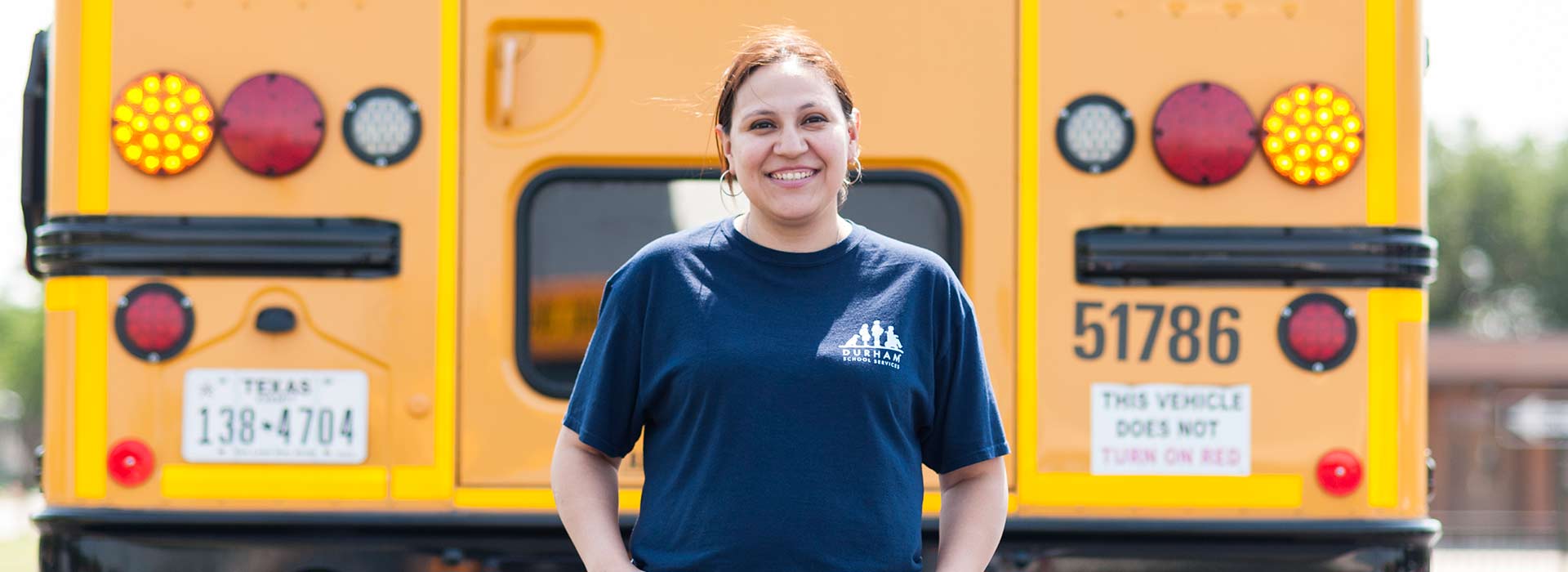 A cheerful female school bus driver standing in front of a school bus