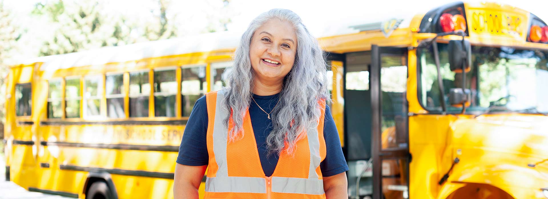 A smiling female bus driver standing in front of a school bus