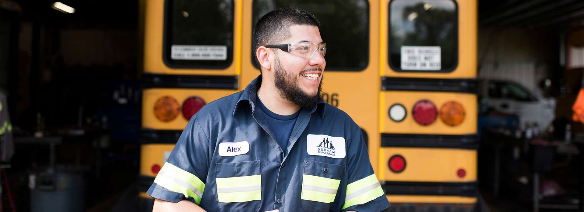 A smiling maintenance technician standing in front of a school bus