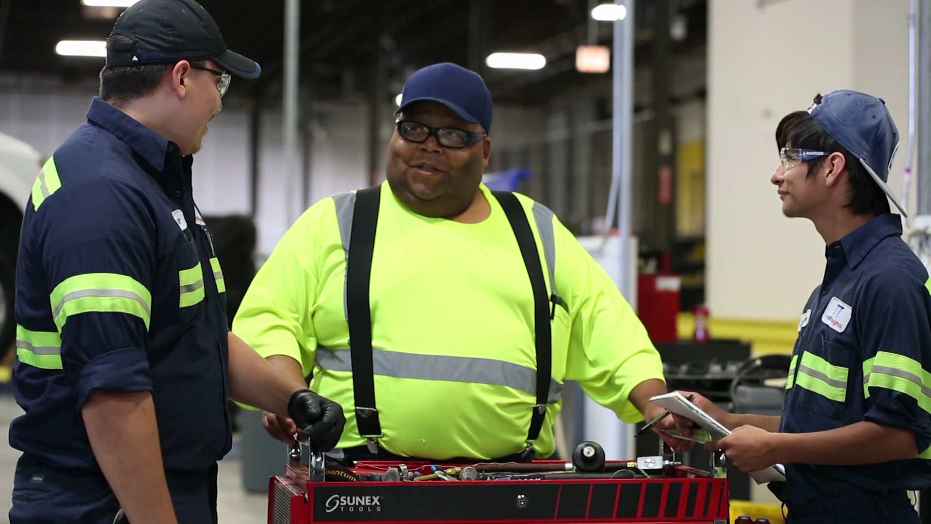 Three mechanics engaged in a friendly conversation, while carrying a set of working tools