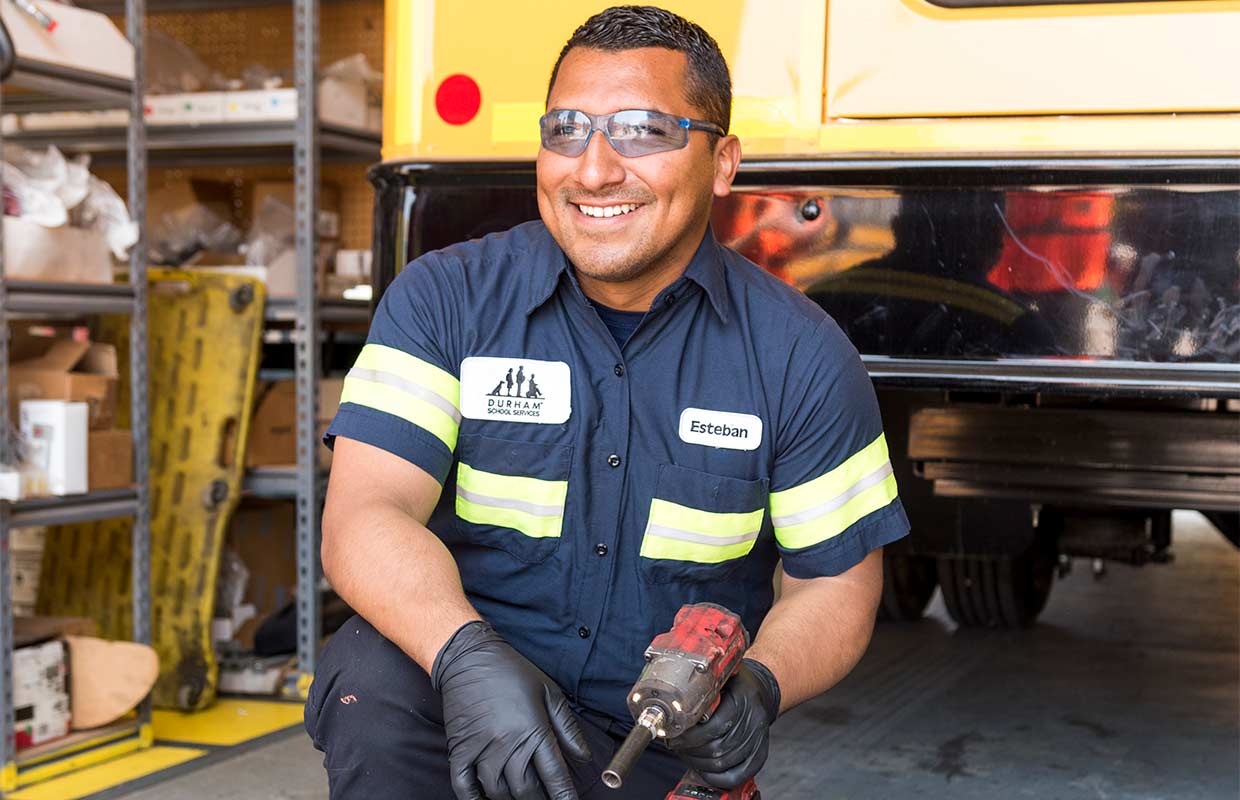 A male mechanic smiling in front of a yellow bus, displaying a focus on passenger safety.