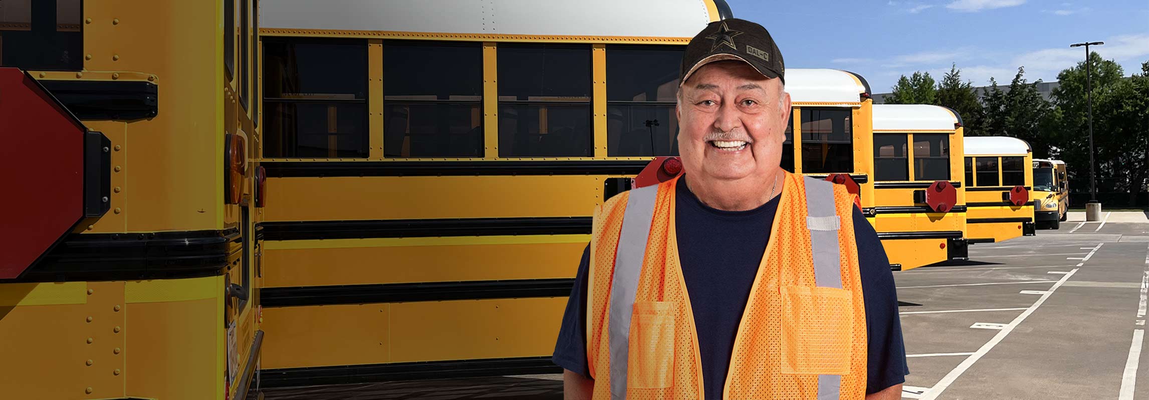 A veteran school bus driver smiling and standing confidently in front of a row of parked school buses, showcasing pride in his work