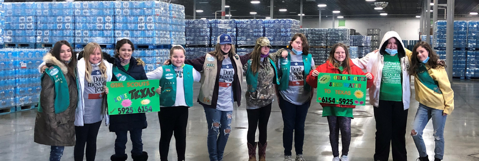 Girl Scout members standing in front of cases of water with "Love Texas" posters