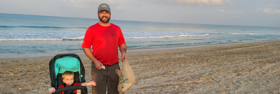 Man with his son in a stroller on the beach picking up trash 