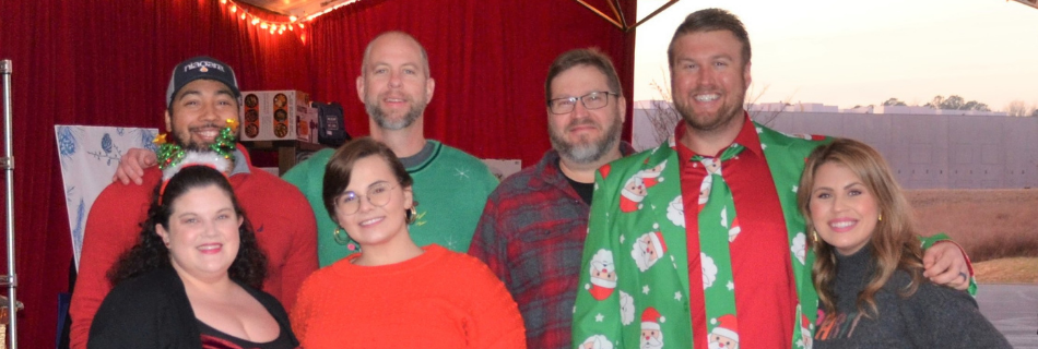 Niagara team members in holiday outfits smiling in front of a red curtain