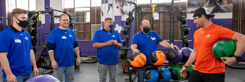 Five men holding weighted balls in a work out facility