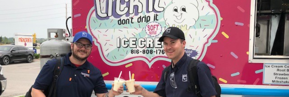 Two men smiling in front of an ice-cream food truck with ice-cream in hand