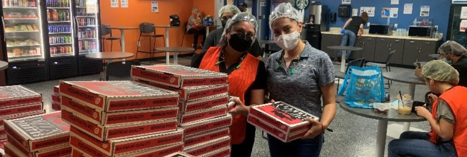 Photo of two Niagara team members in plant gear (mask, vest, and hair net) with several boxes of pizza