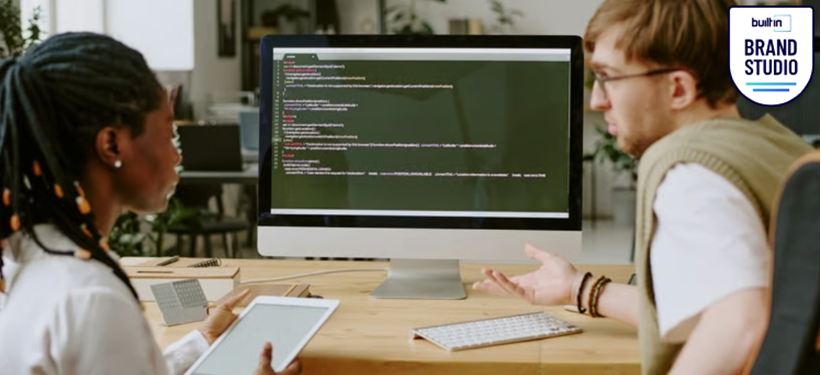 Two people sitting in front of a computer screen with code showing.
